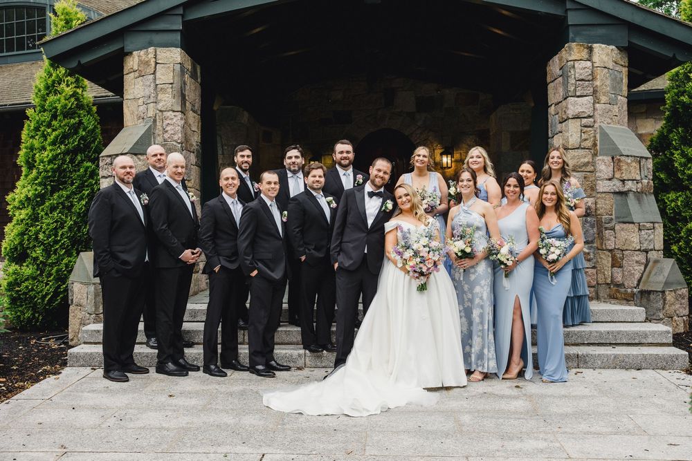 Wedding party poses together on stone steps for formal group photos in elegant attire.