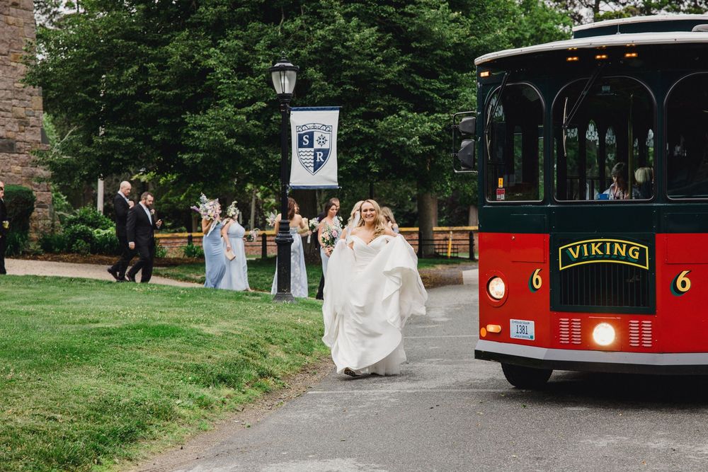 A wedding party rides in a red trolley bus through a scenic park setting on their special day.