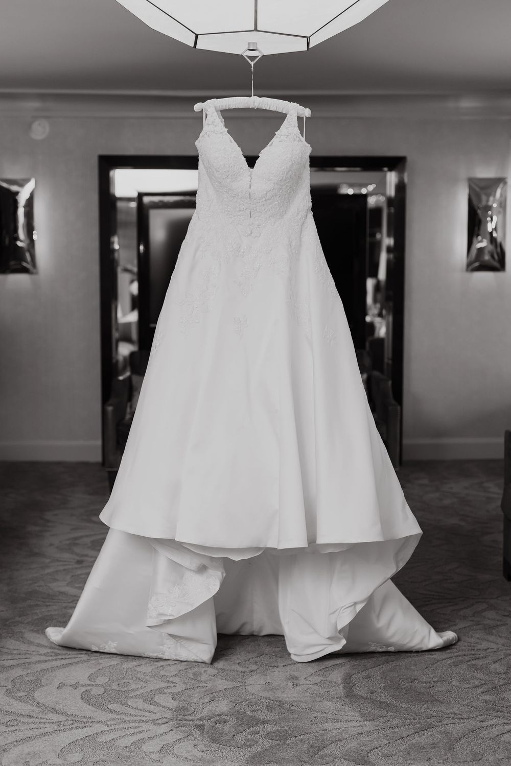 Floor-length white wedding dress with flowing skirt photographed against dark carpet in black and white.