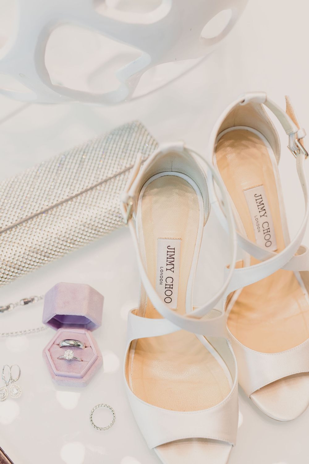 Elegant white bridal shoes with crystal embellishments displayed on a textured surface.