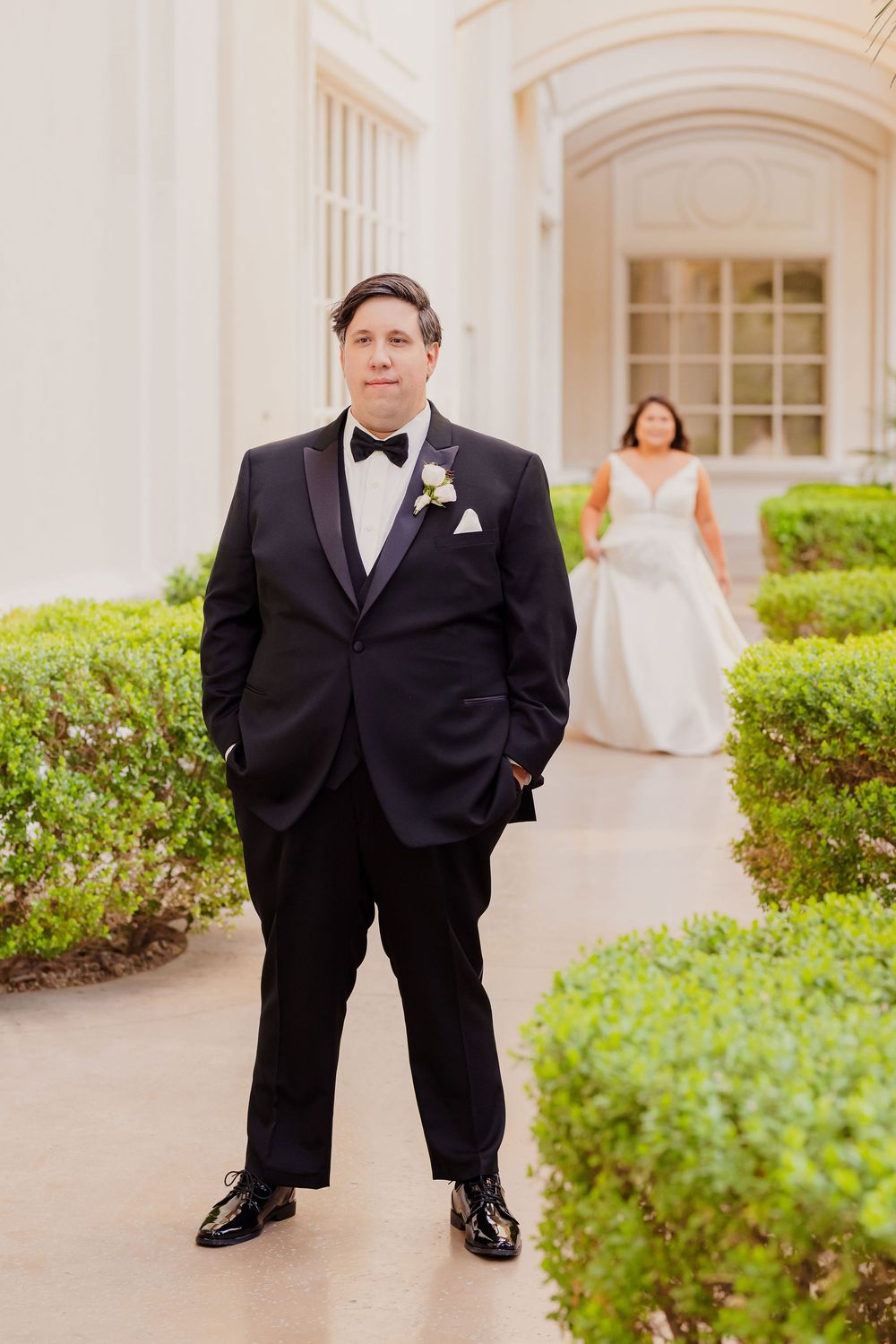 Wedding couple posing in front of a classic white building with manicured hedges.
