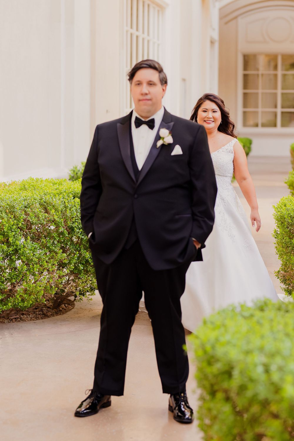 Bride and groom share a playful moment in front of a columned building with landscaped grounds.