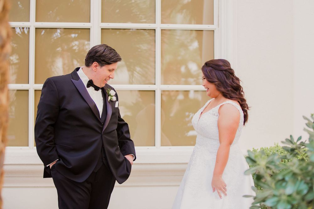 A couple in formal wedding attire shares a romantic moment together in front of a window-lined building.