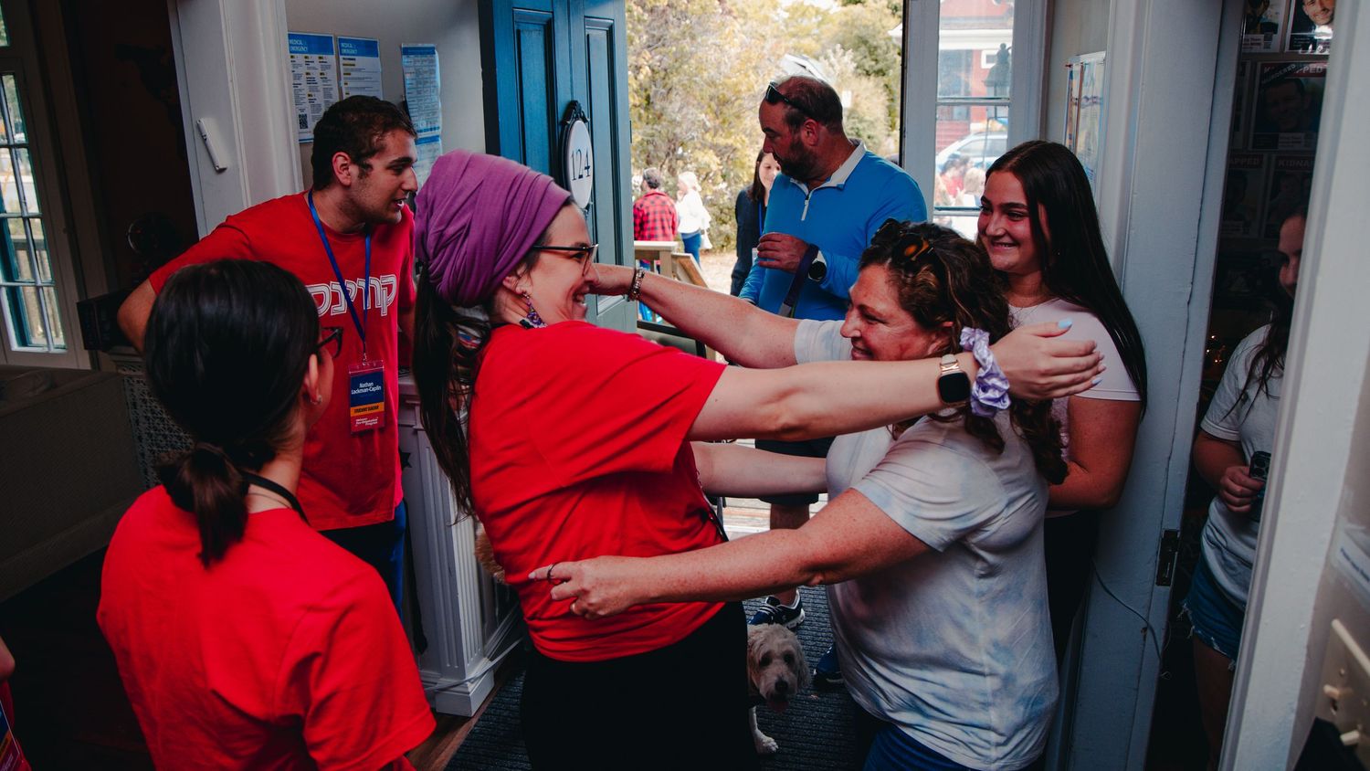 People in red and blue clothing gather in a hallway for group photos during a social event.