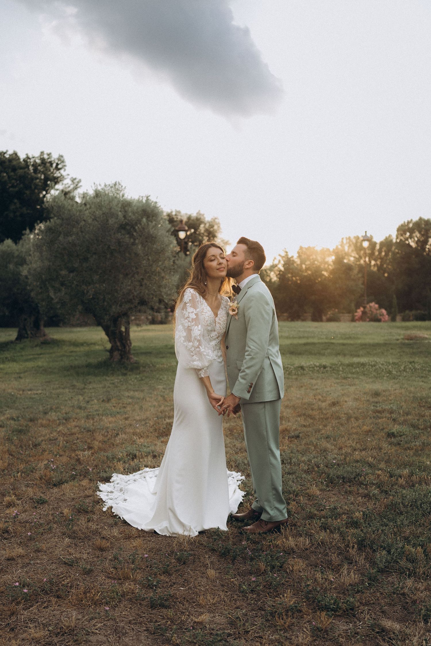 Romantic embrace in golden wheat field under cloudy sky.
