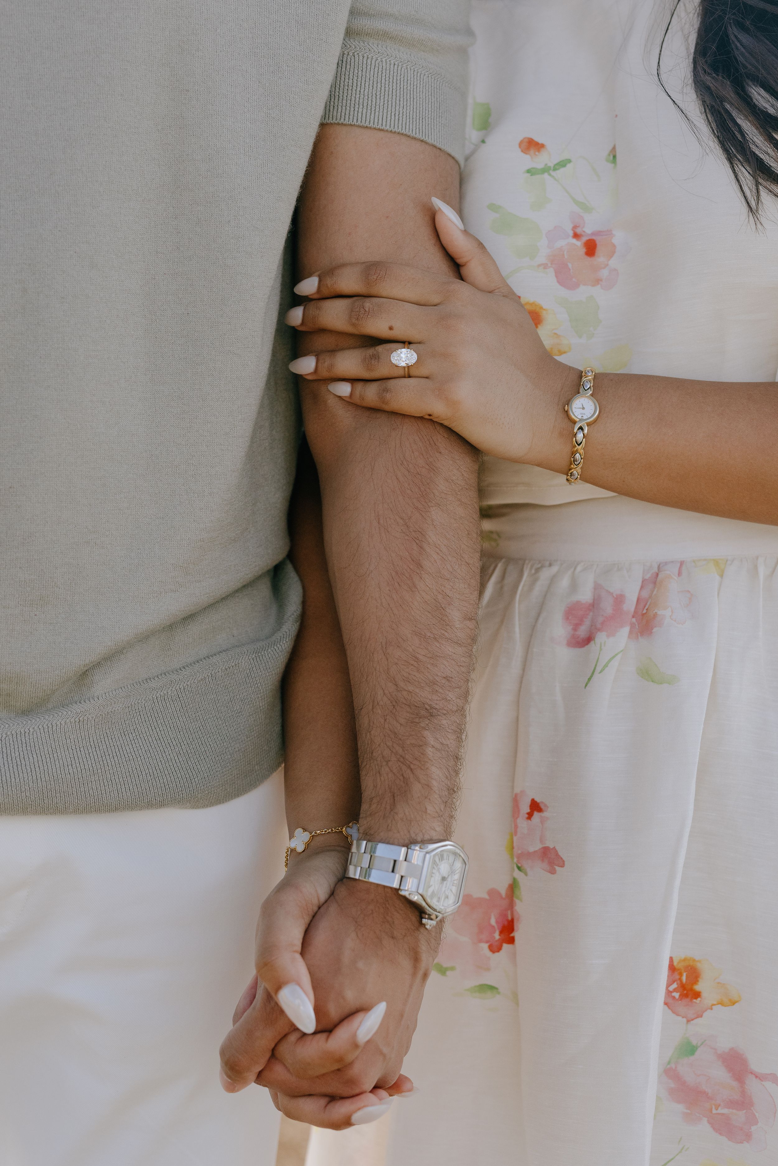 Close-up shots of hands wearing engagement rings and wedding bands against a light floral dress background.