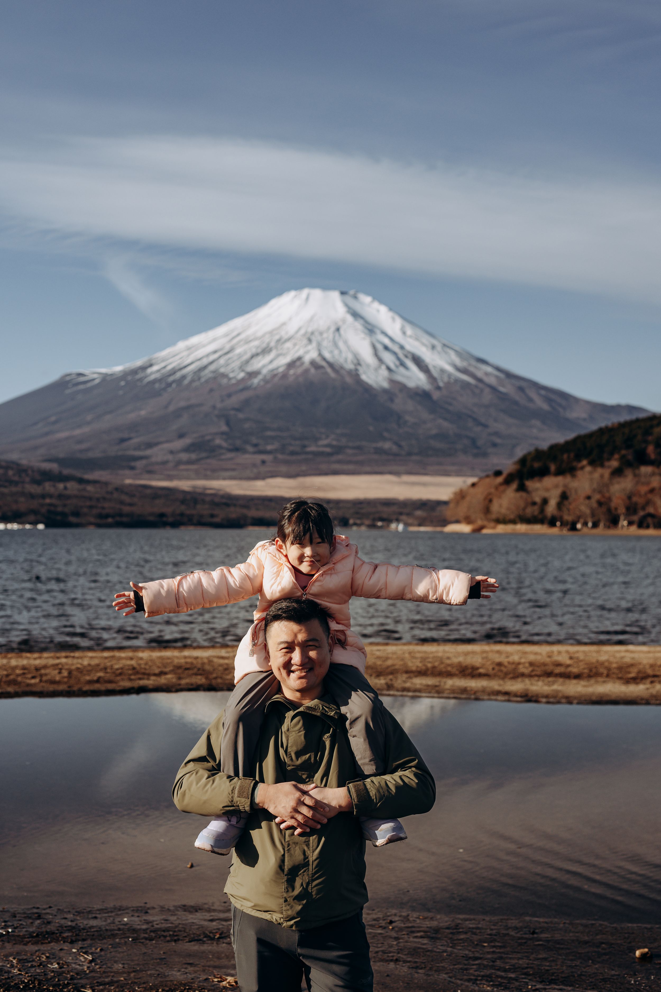 Two people enjoying a scenic moment at Lake Yamanaka with snow-capped Mount Fuji rising majestically in the background.