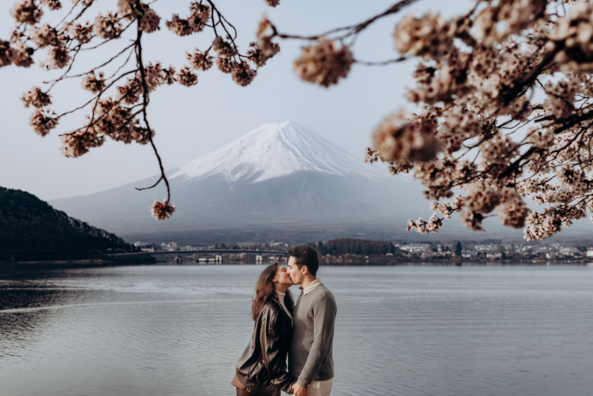 Cherry blossoms frame a scenic view of Mount Fuji and Lake Kawaguchiko in Japan during spring season.