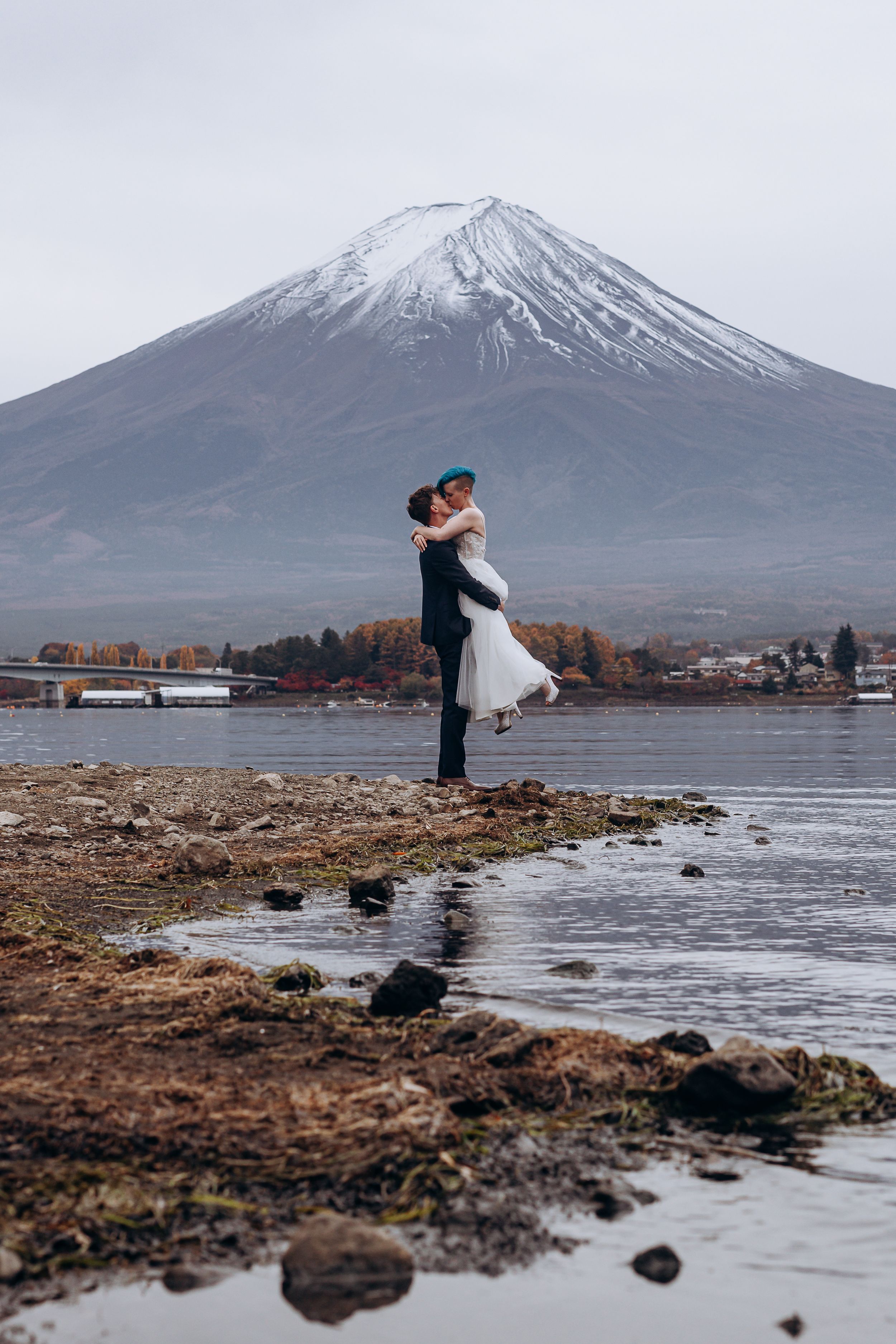 A couple poses for romantic wedding photos against the majestic snow-capped Mount Fuji and Lake Kawaguchiko in Japan.
