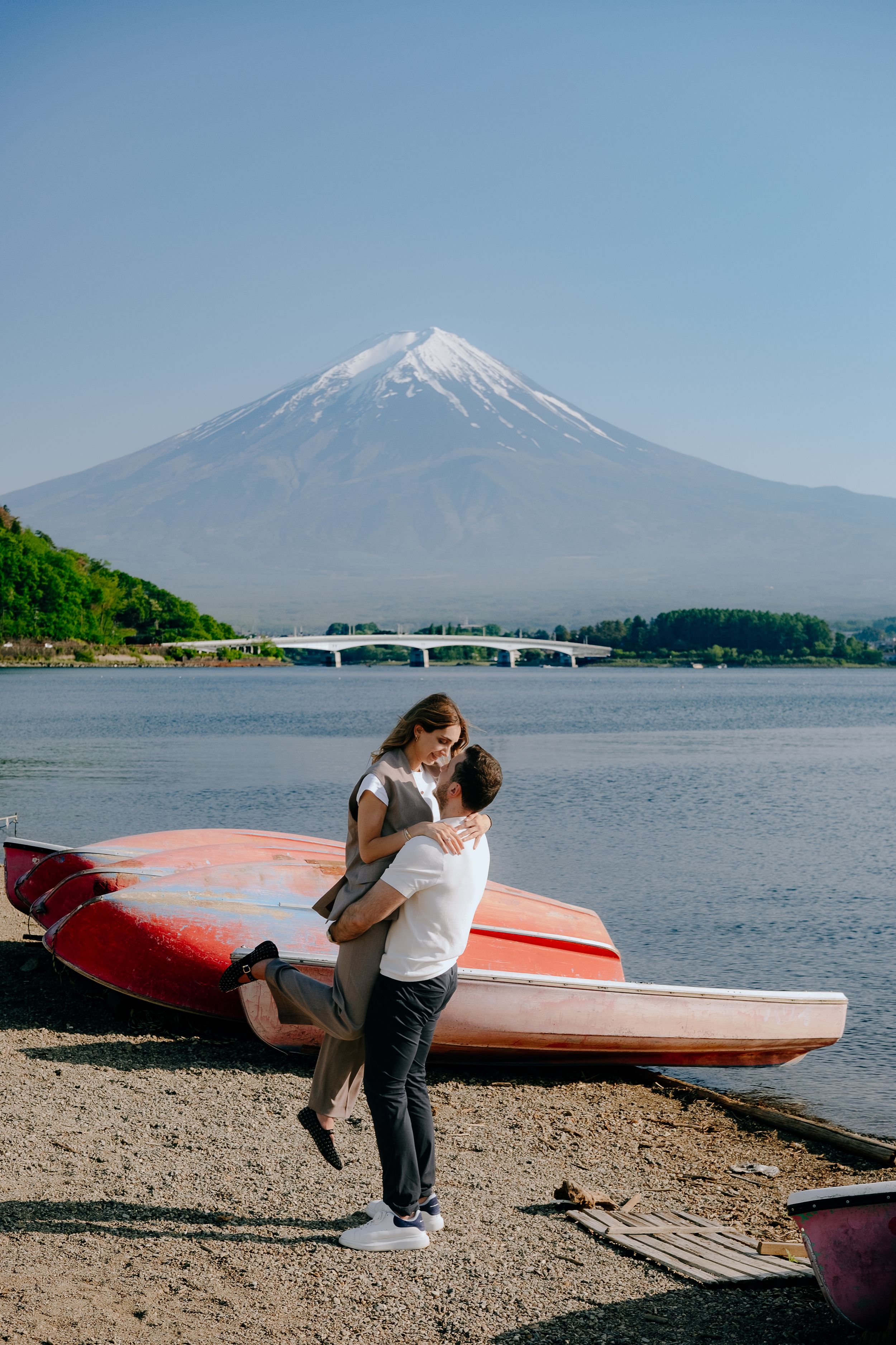 Couple embracing and kissing on the shore of Lake Kawaguchi with iconic snow-capped Mount Fuji in the background, Japan.