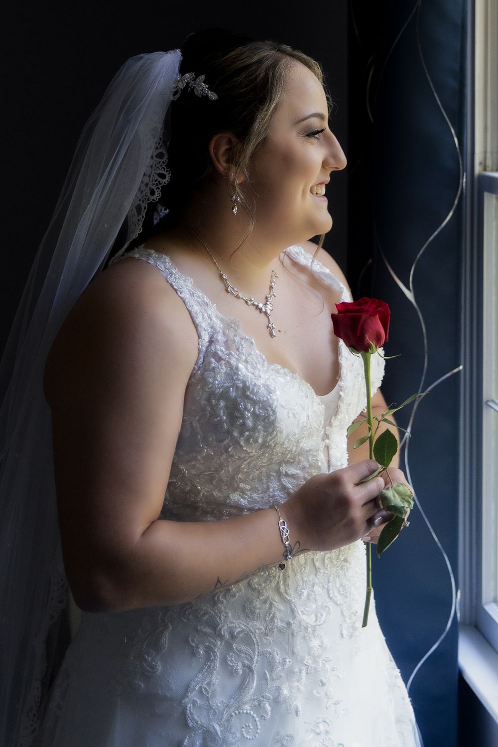 A series of profile shots showing a bride in a white lace dress holding a red rose by a window.