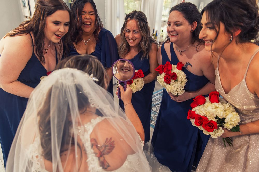 A joyful wedding party gathers around the bride in navy blue dresses while sharing smiles and laughter.