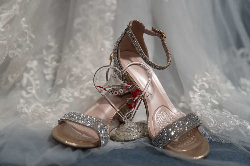 A row of elegant bridal shoes with sparkly embellishments and delicate straps displayed against white lace fabric.