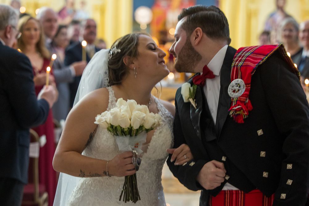 A romantic wedding couple shares a tender kiss during their reception dance while guests look on in the background.