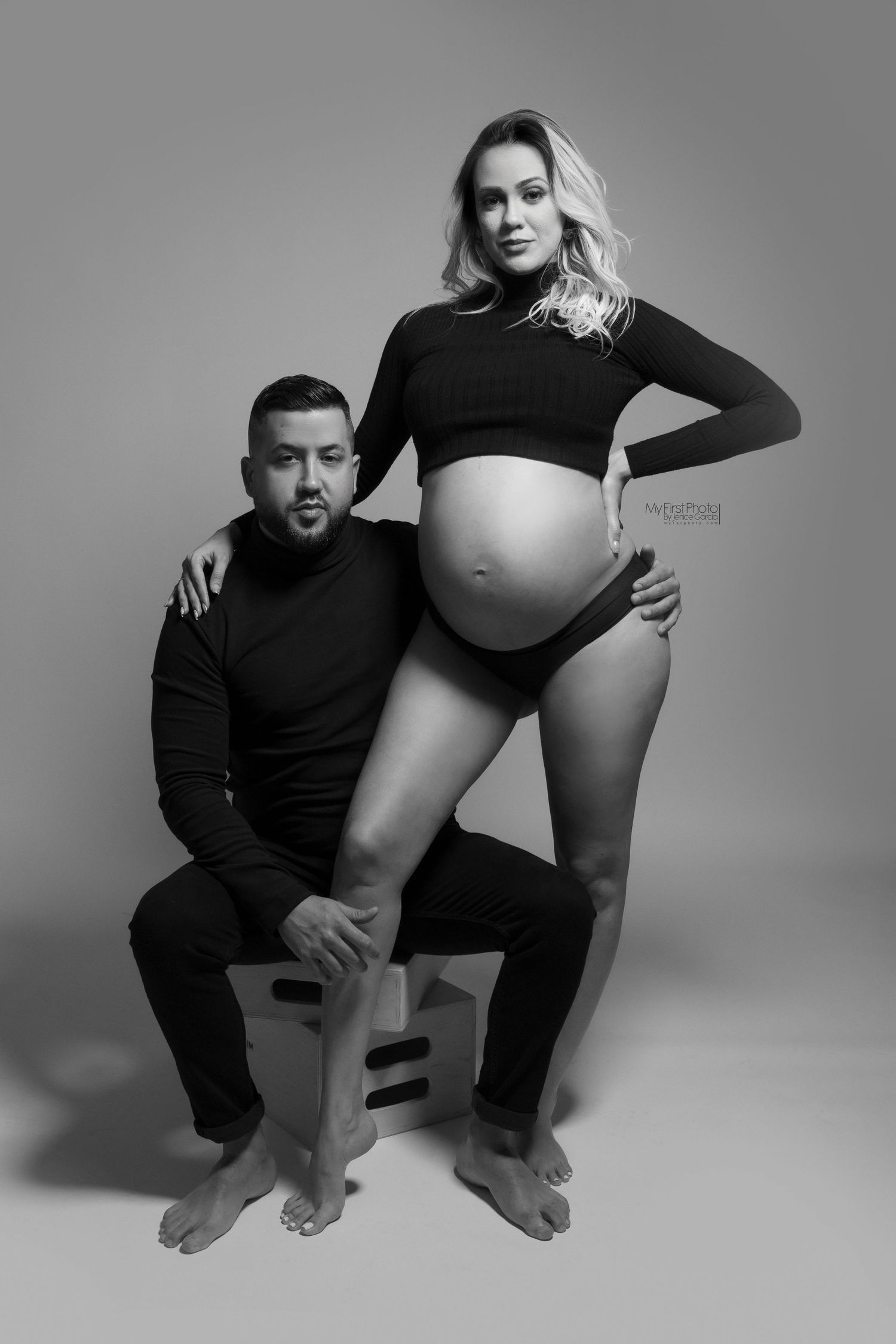 Black and white maternity photo series showing couple in intimate poses against light background.