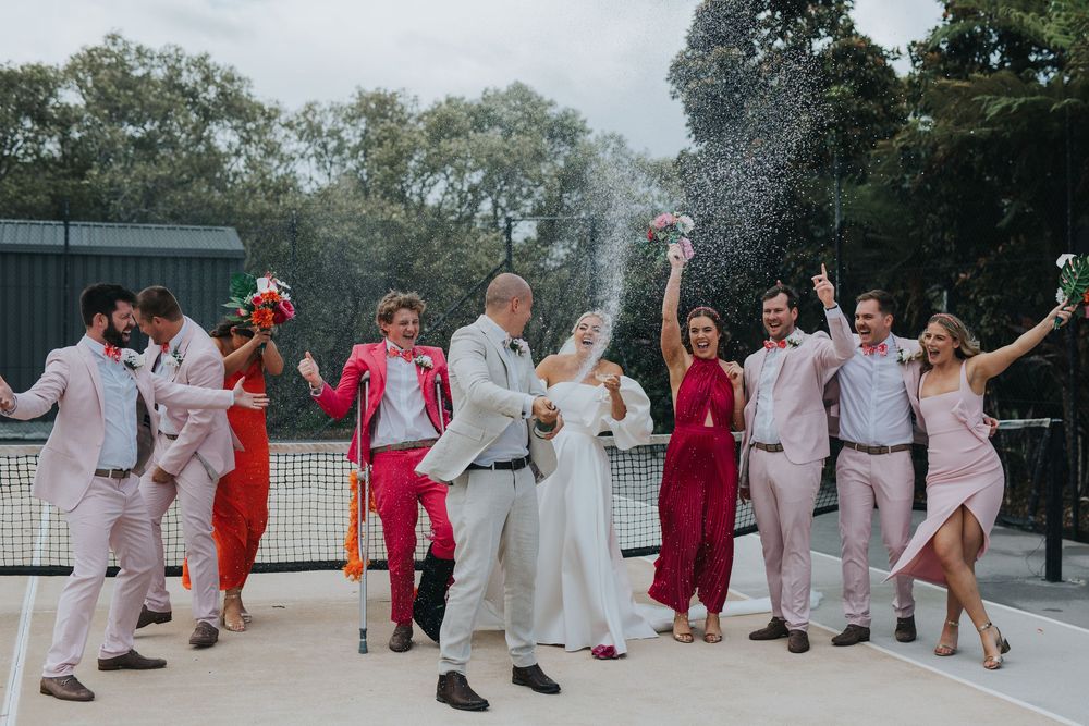 Wedding party members in red and white attire dance together in a joyful outdoor celebration.