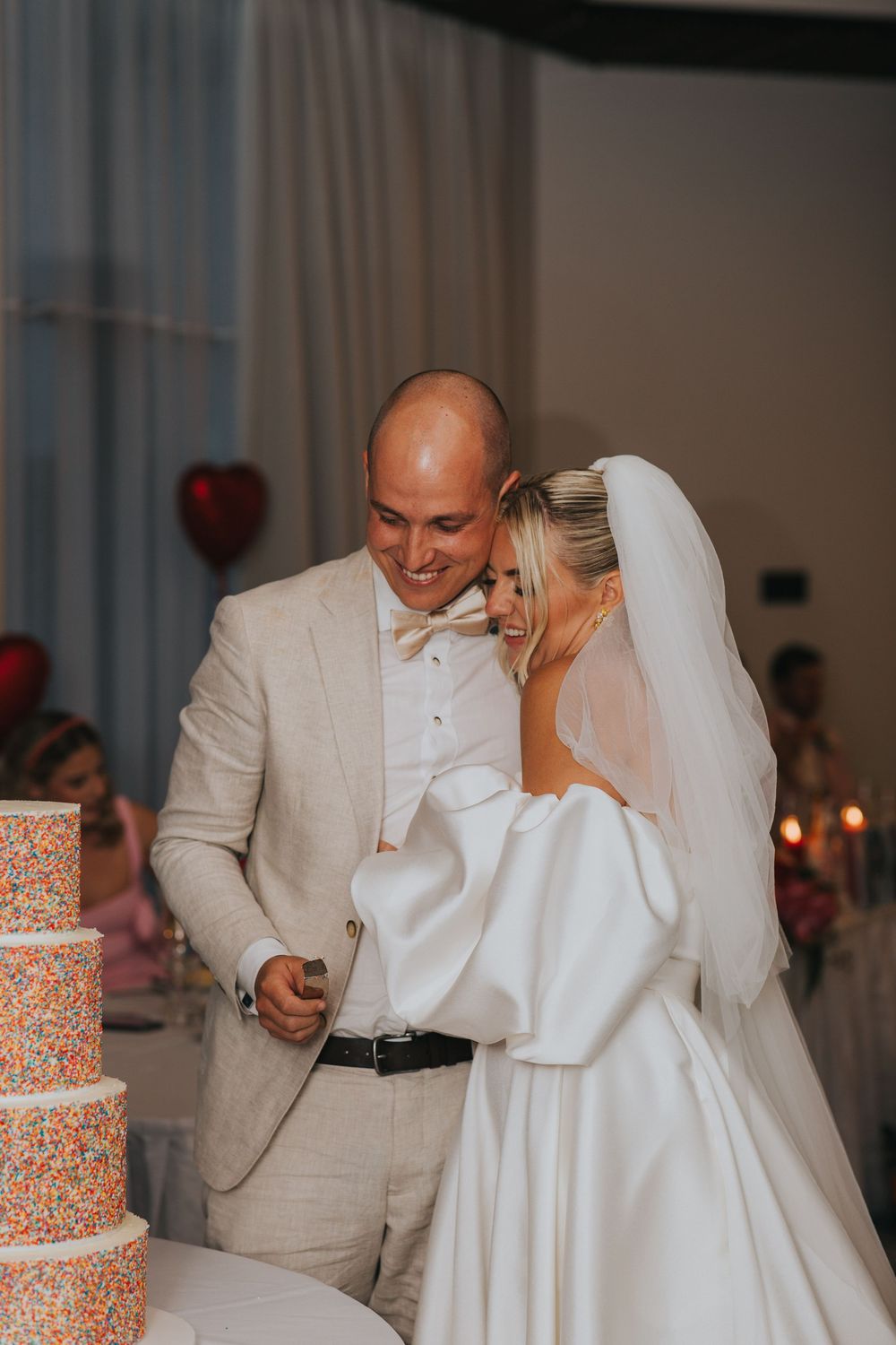 A bride and groom share a sweet moment together while cutting their orange and white floral wedding cake at their reception.