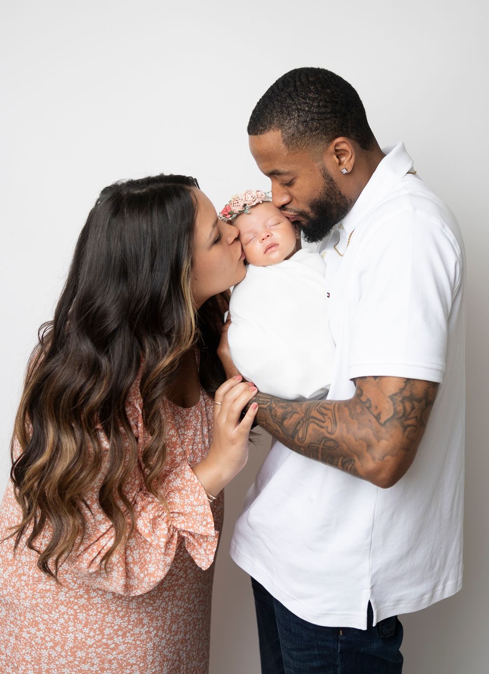 Family shares tender moments in matching white and pink outfits against neutral background.
