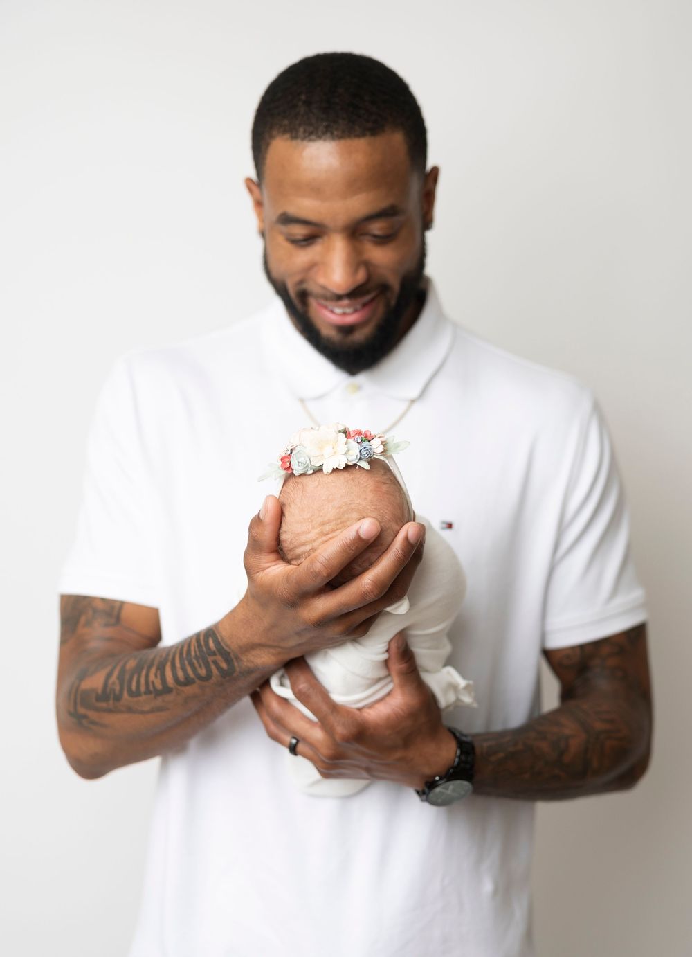 Person in white t-shirt with tattoos holds and smiles at a decorated cupcake against a light background.