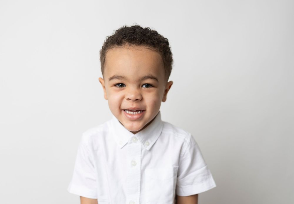 A young child in a white polo shirt smiles and poses against a white background in a series of four photos.