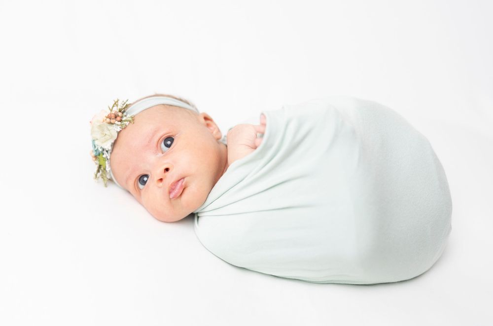 Newborn baby wrapped in mint green swaddle blanket lying on white background.