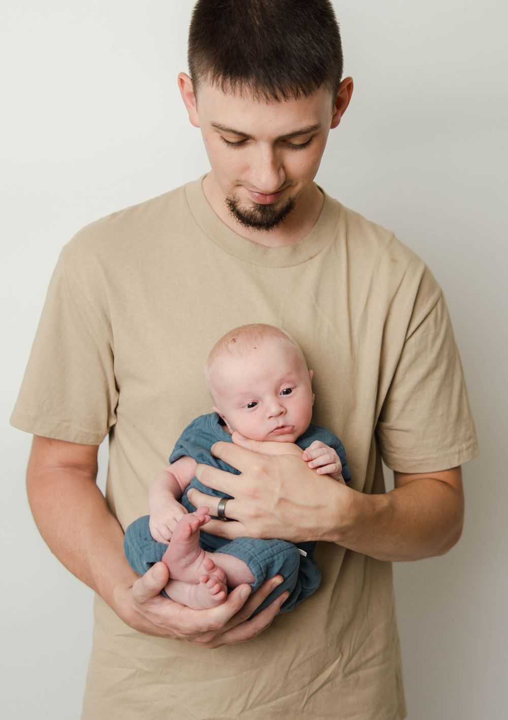 A tender moment shows a parent in a beige t-shirt gently cradling a small baby wearing blue clothing.