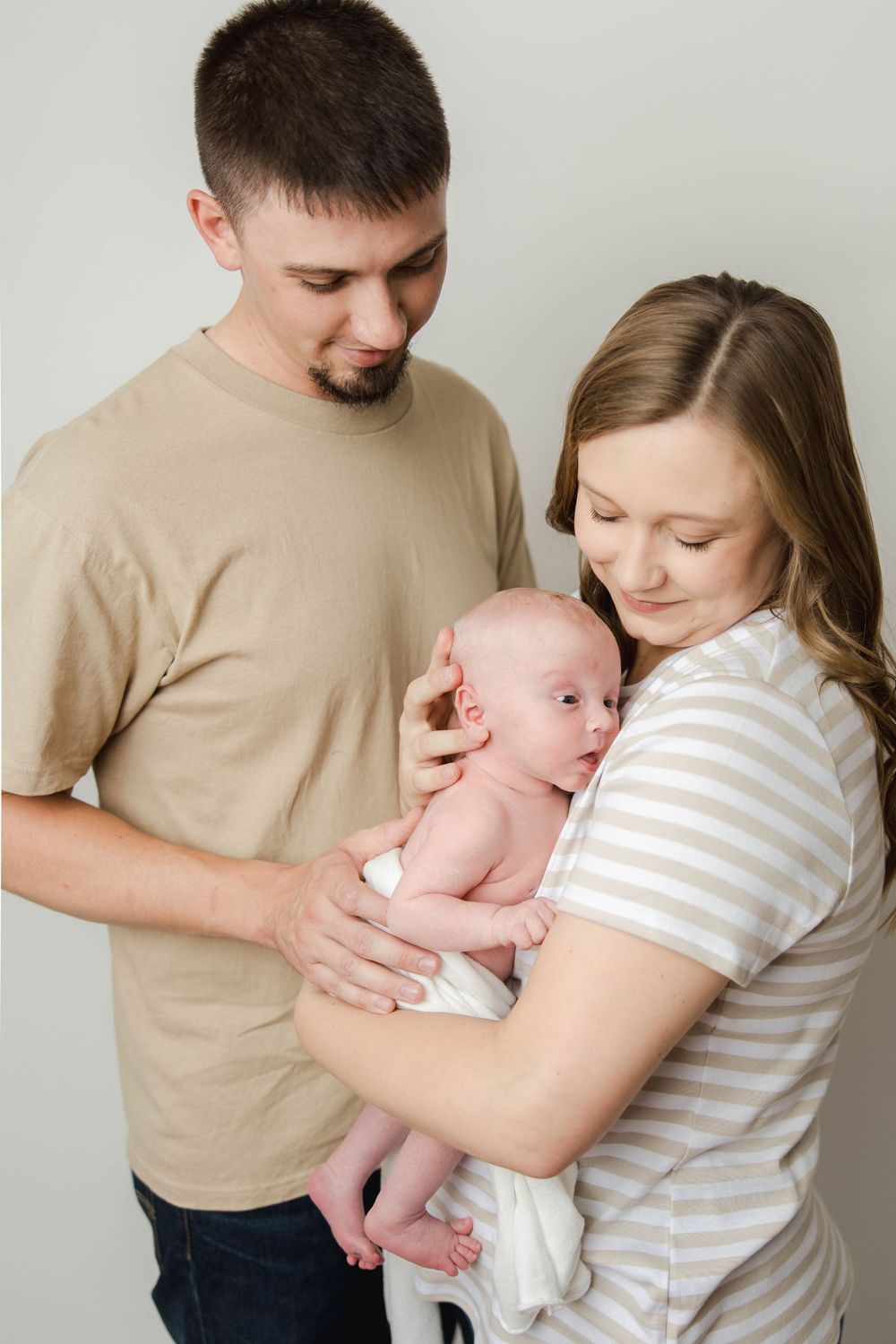 A series of tender moments between parents and their baby in a minimalist studio setting against a light background.