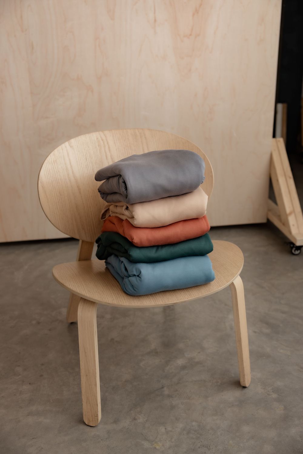 Stack of folded colorful clothes in gray, beige, rust, green, and blue on a modern wooden chair.