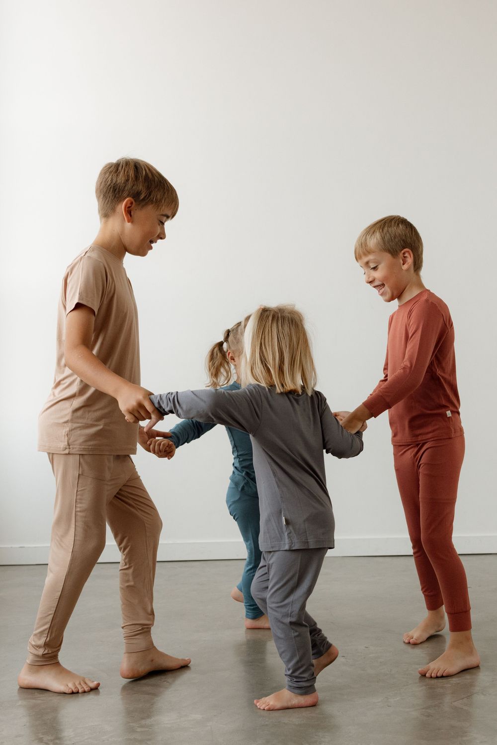 Three children in matching pajamas hold hands in a circle, playing together on a light gray floor.