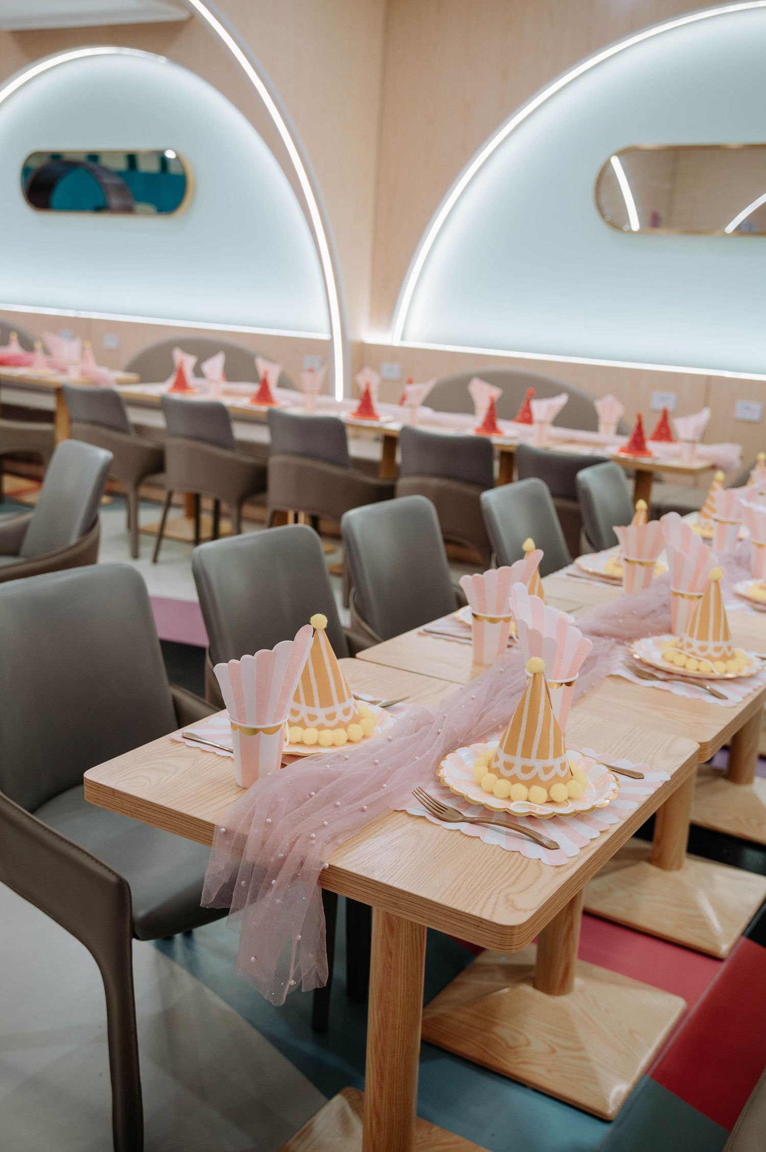 Party table settings with pink tulle runners and gold party hats in an event space.