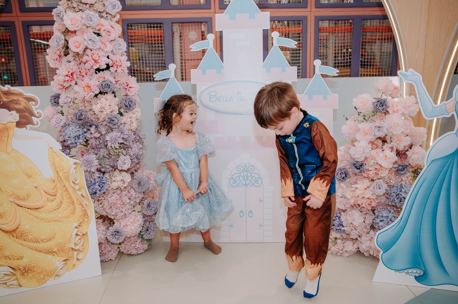 Two children playing in front of a fairy tale castle backdrop with pink floral decorations.