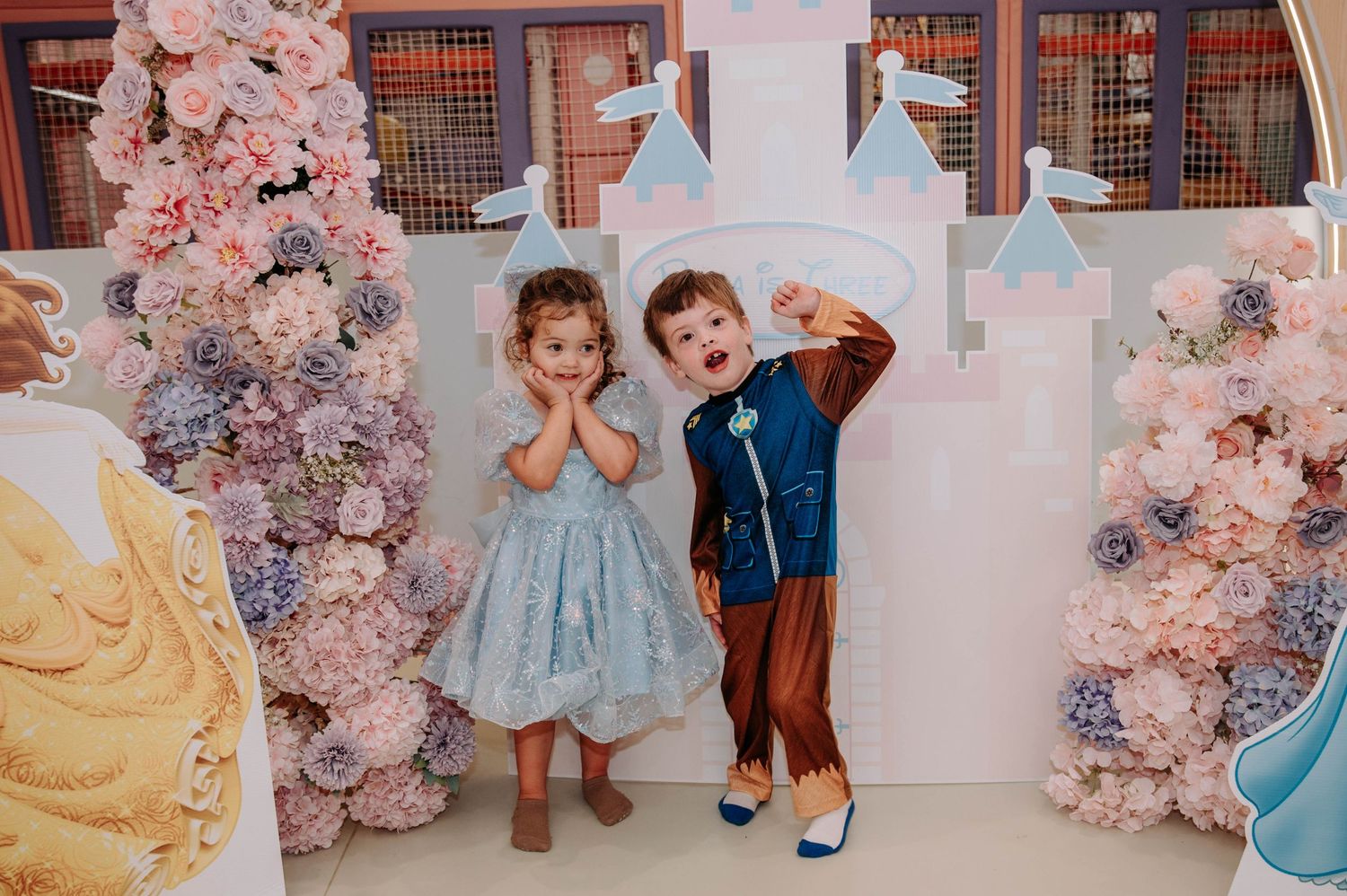 Children pose in front of a pink floral princess-themed backdrop with castle decorations.