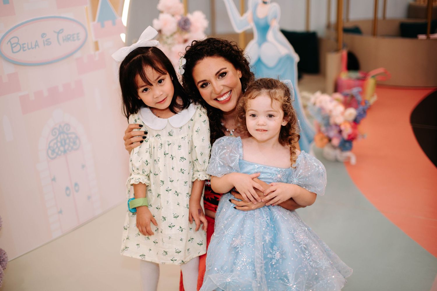 Children posing together at a princess-themed party with Disney character decorations and pink florals.