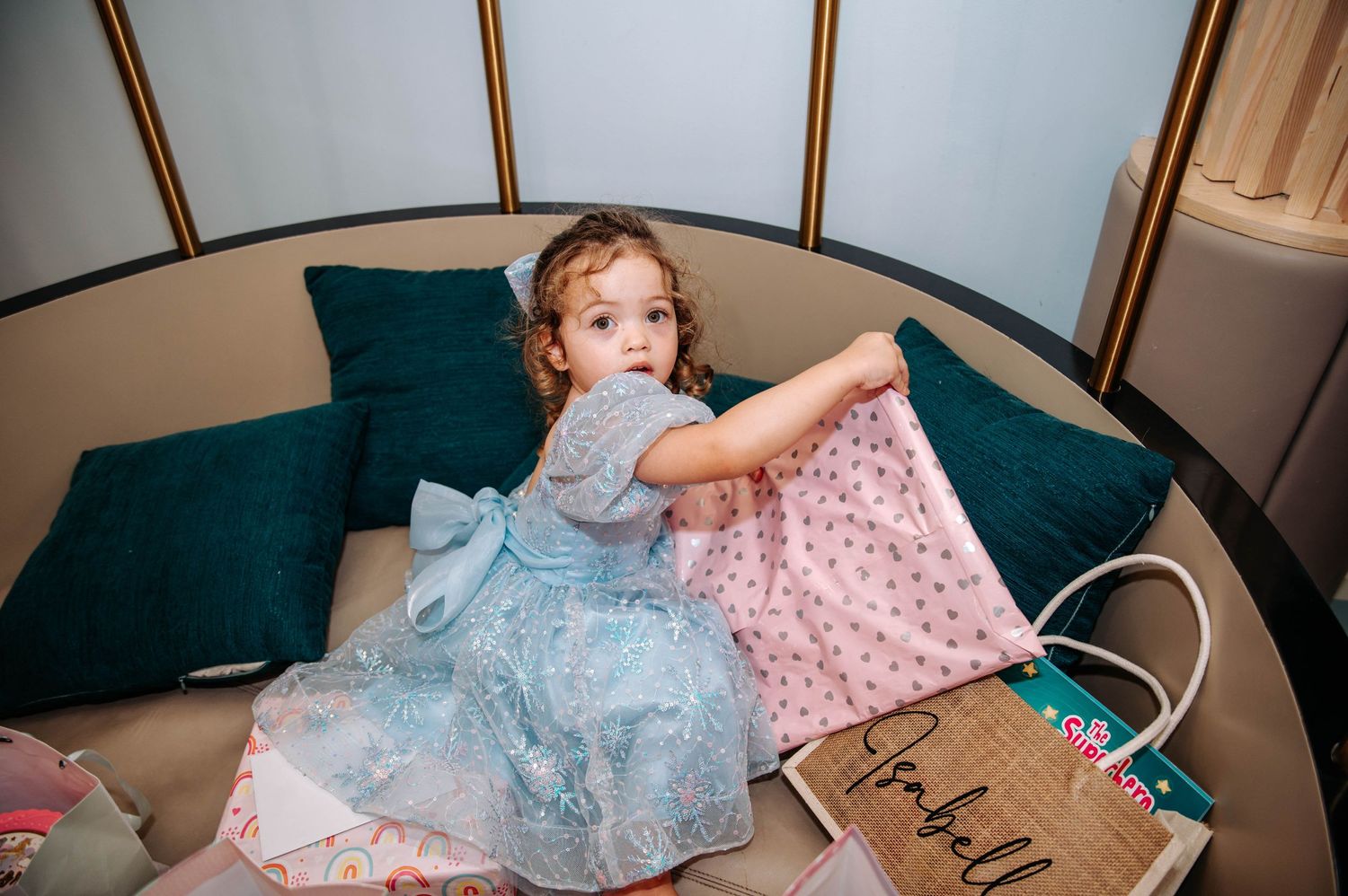 A child in a blue princess dress relaxes on teal cushions during a themed photoshoot.