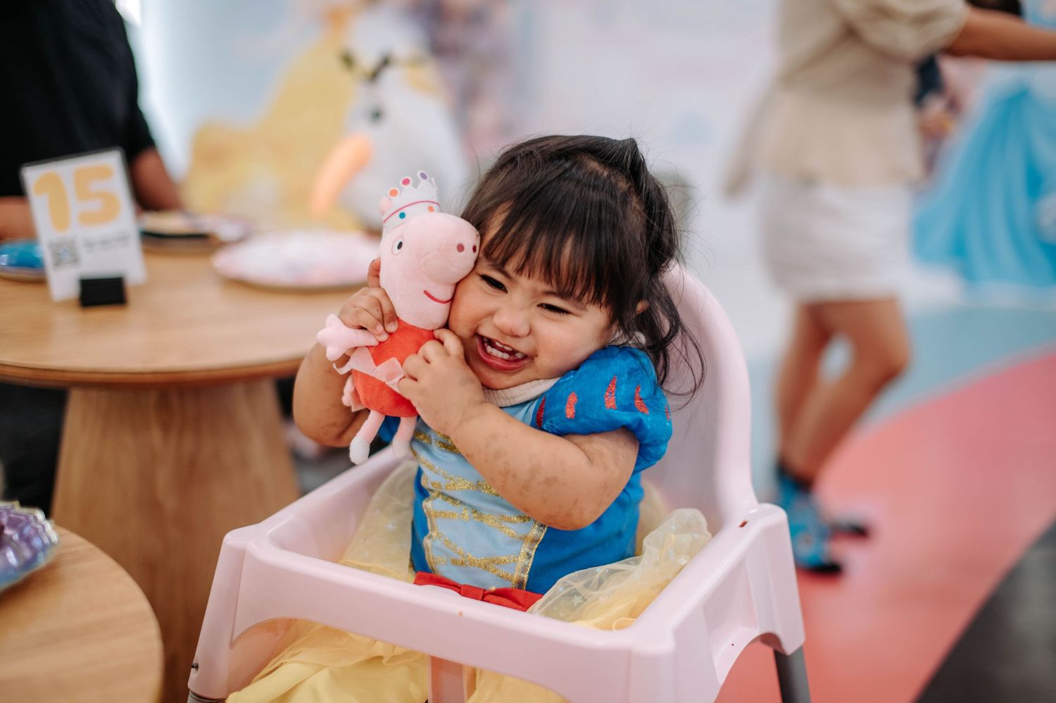 A happy child in costume plays with a pink plush toy during a princess-themed celebration.