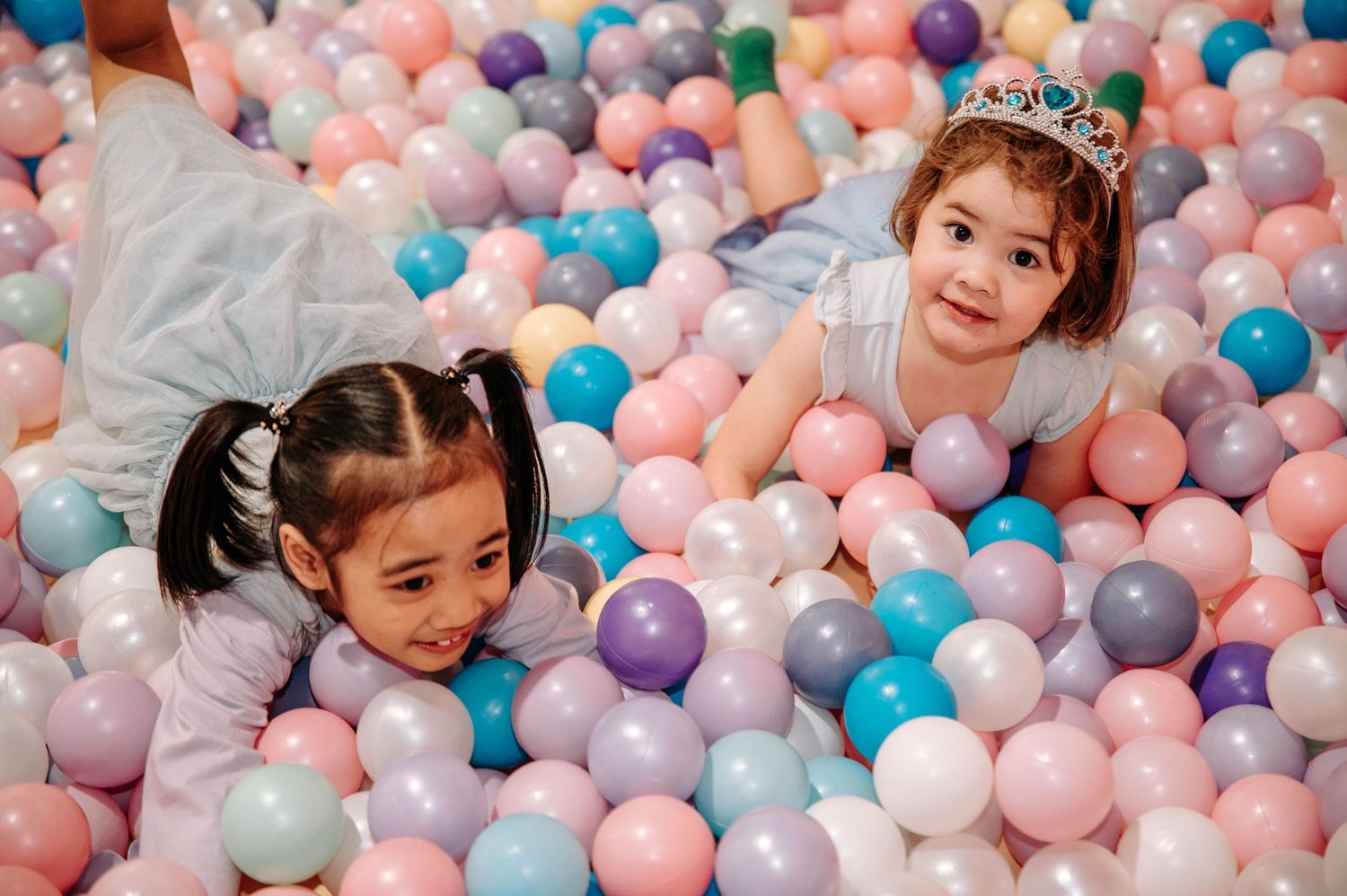 Happy children playing in a colorful ball pit filled with pastel balloons.