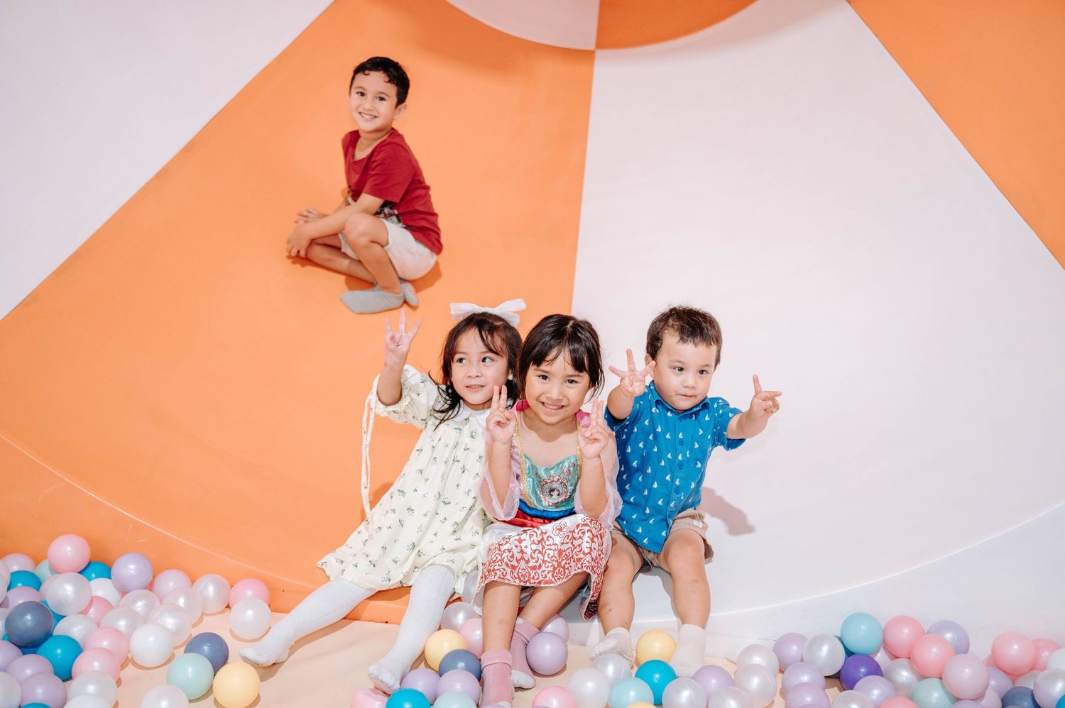 Children playing and posing against an orange and white backdrop with pastel balloons.