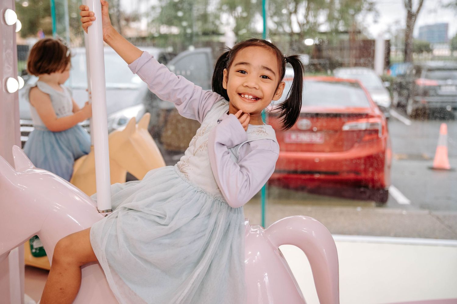 Child riding on a pink carousel horse with joyful expression.