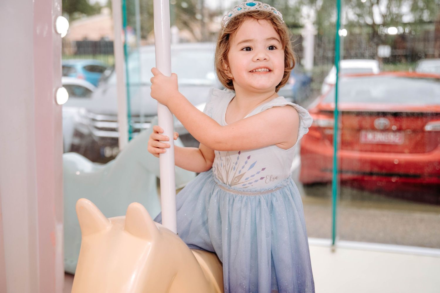 Child in a light blue dress enjoying a carousel ride outdoors.
