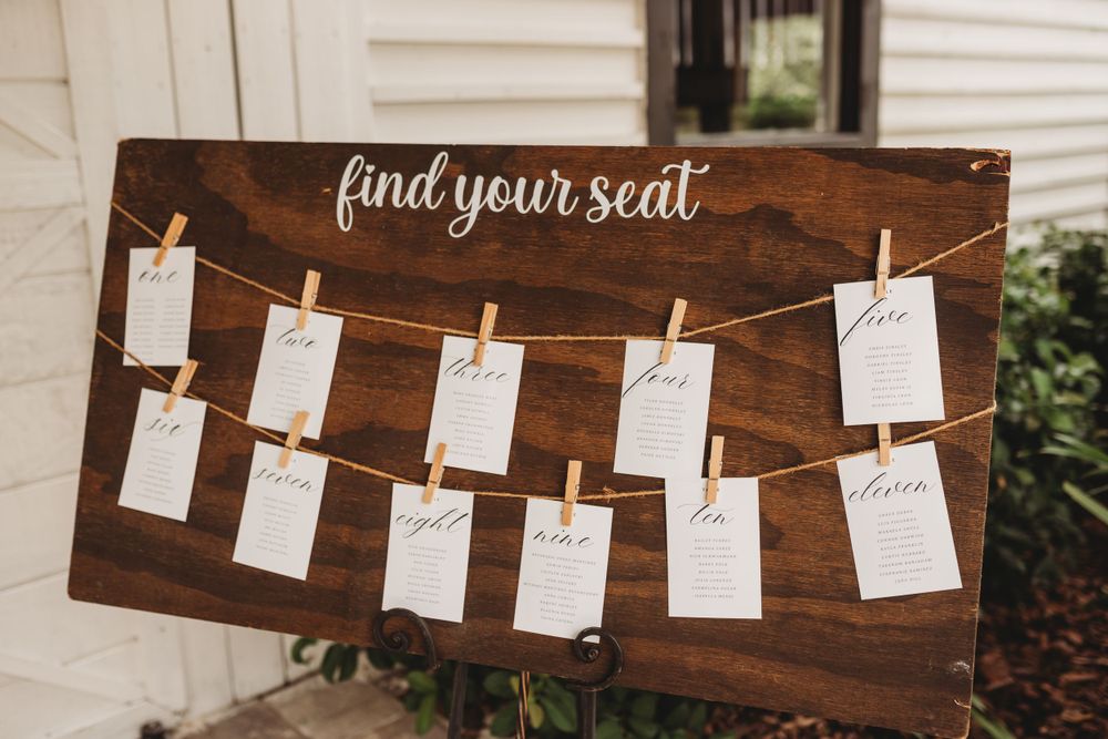 A rustic wooden seating chart display with cards hanging on string with clothespins.