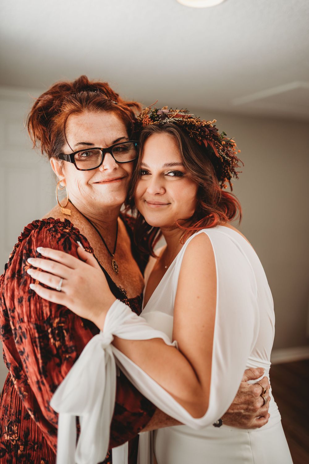 Two women share an intimate embrace while wearing wedding attire indoors.