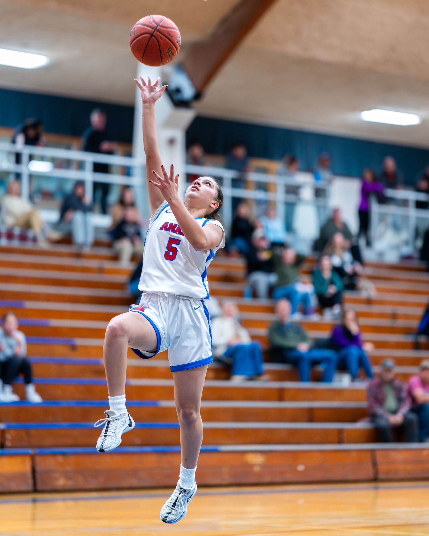 Basketball player leaps high to make a shot during game in school gymnasium.
