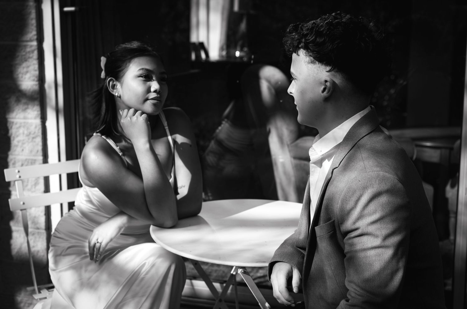Black and white romantic portrait of couple having intimate conversation at cafe table.