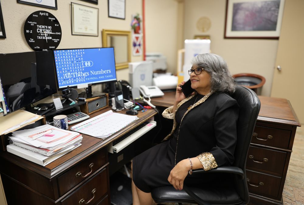 A professional working at a desk with computer monitors and office equipment.