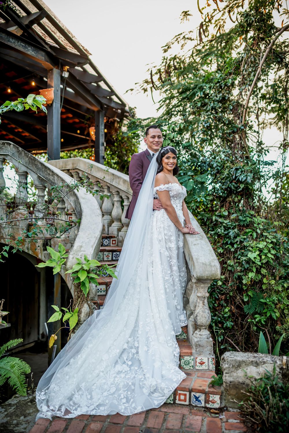 A stunning wedding dress with intricate lace detail and flowing train against stone architecture.