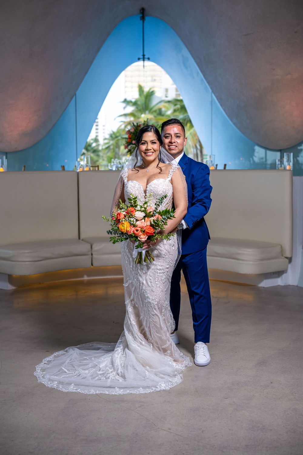 Elegant wedding couple poses under modern blue and white architectural dome.