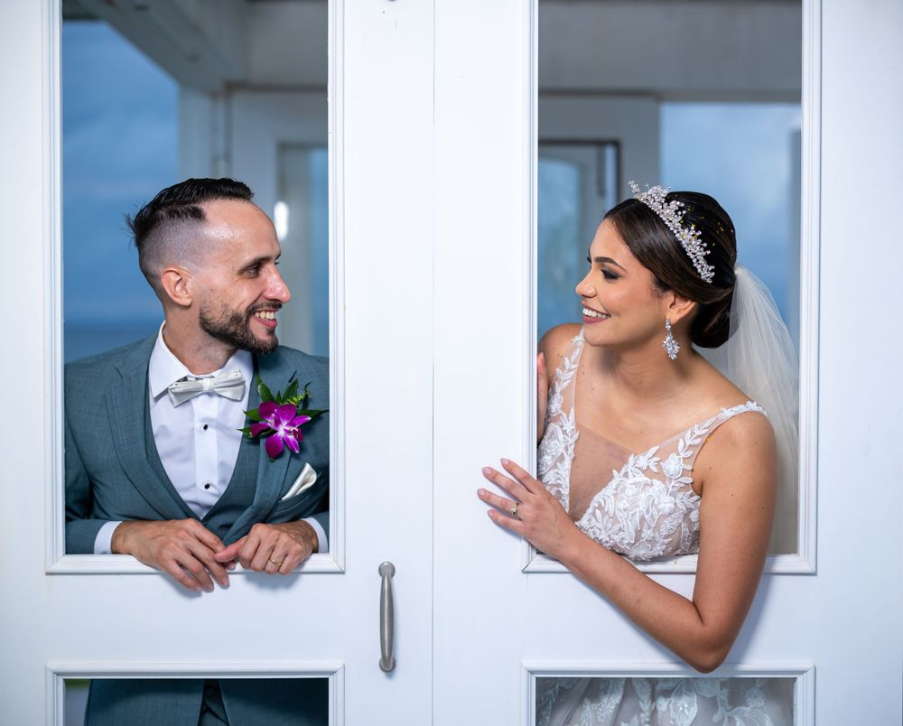 Playful wedding portrait through white window frames showing couple's joyful interaction.