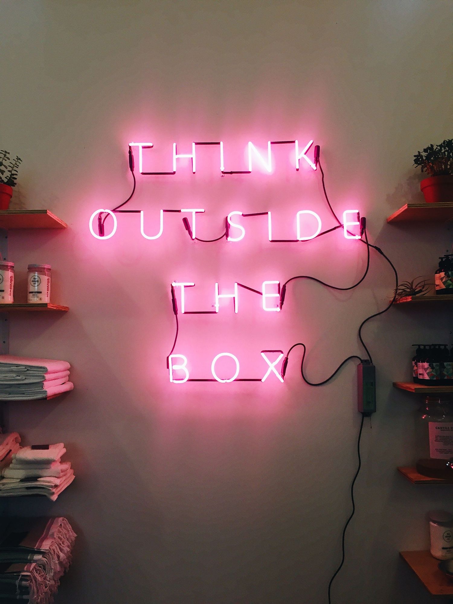 A picture of a pink neon sign that says, "Think outside the box".