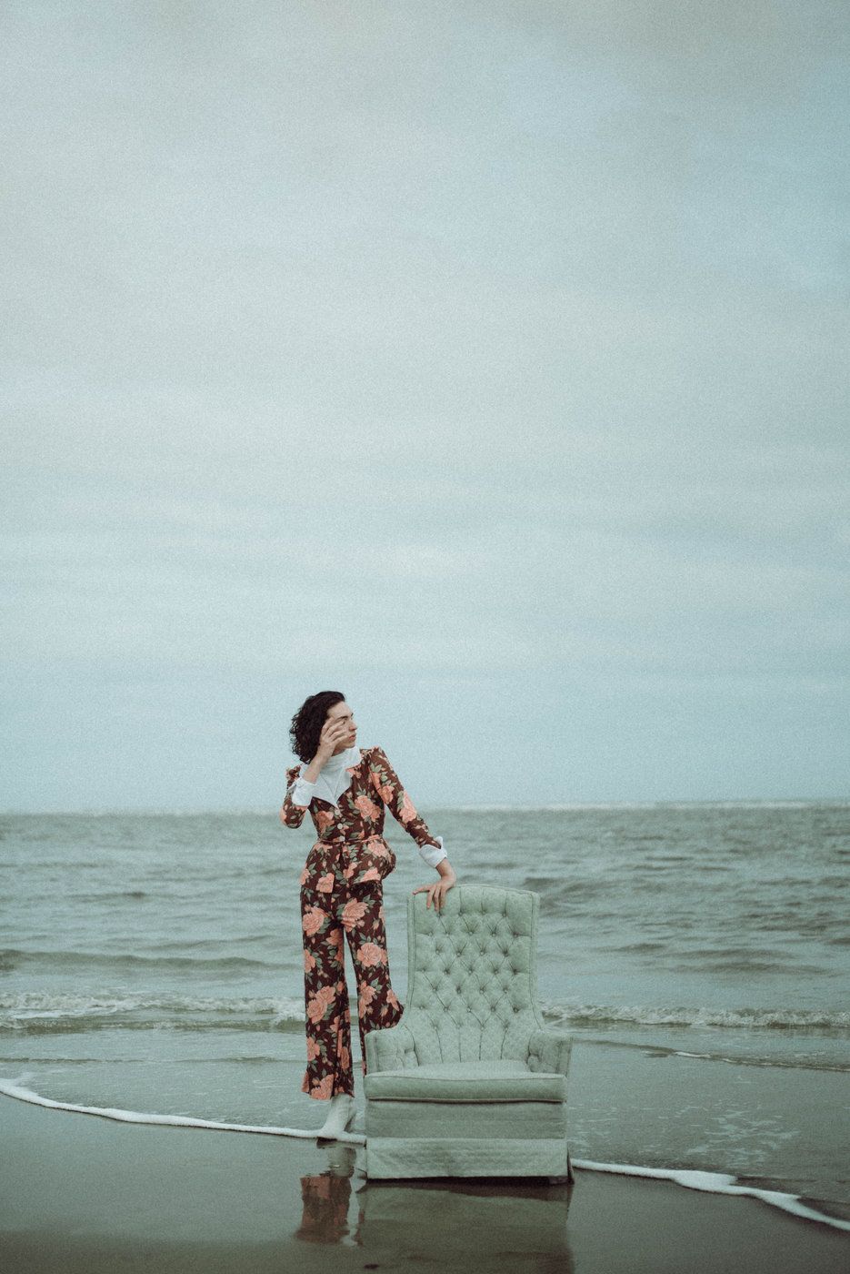 A portrait of a person touching a chair while standing on the beach.