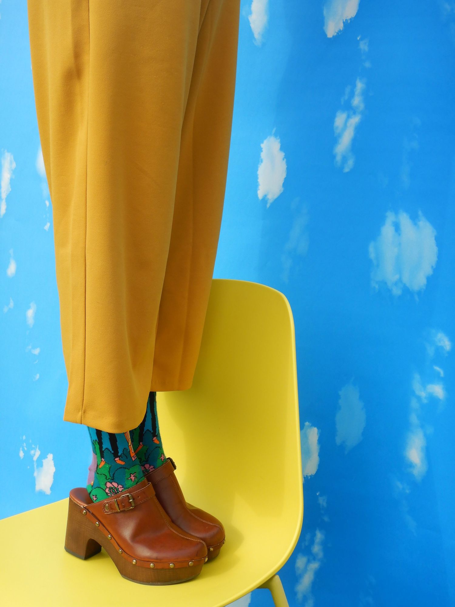 A portrait of someone standing on a chair with yellow pants on.